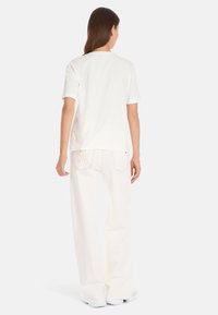 Witte katoenen t-shirt met korte mouwen, ronde halslijn en een relaxte pasvorm, gecombineerd met off-white wijde broek en witte schoenen.