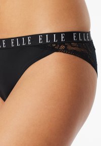 Zwarte thong met kantafwerking en een zachte tailleband met "ELLE" branding. Glad stof met een strak ontwerp dat de rondingen accentueert.