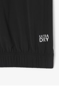 Tejido atlético negro con un dobladillo elástico fruncido. Presenta "ULTRA DRY" impreso en blanco cerca de la parte inferior, indicando propiedades de absorción de humedad.