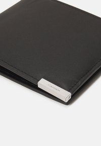 Portafoglio in pelle nera con una texture liscia, caratterizzato da un accento metallico argentato impresso con "Calvin Klein" sul bordo.