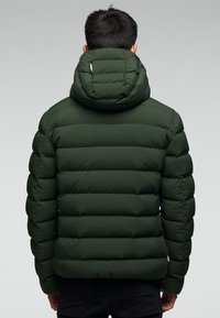 Zelená prošívaná bunda s vysokým límcem a kapucí, svislé prošívané části a logo na levé straně.