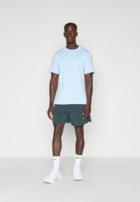 Heledsinine lühikeste varrukatega T-särk ümmarguse kaelusega, kombineeritud tumeroheliste lühikesed pükstega. Valged spordijalatsid ja sokid mustade logo aktsentidega.