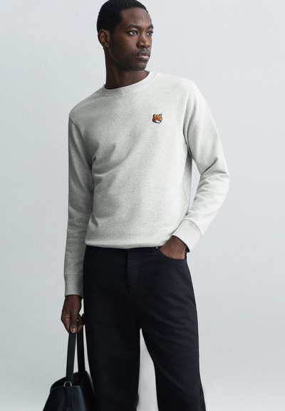 Grijze fleece sweatshirt met lange mouwen, ronde halslijn en een klein geborduurd dierenontwerp; gecombineerd met zwarte broek en een zwarte handtas.