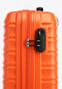 Valise rigide orange avec une surface texturée, une fermeture éclair avec des accessoires noirs et un cadenas à combinaison pour la sécurité.