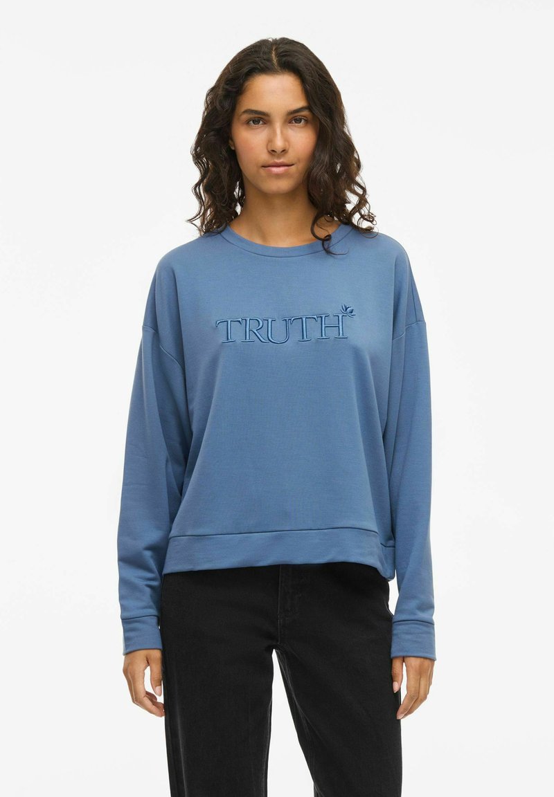 Blå sweatshirt med broderad texten "TRUTH" och en bladdesign. Har en avslappnad passform, manschetter vid ärmarna och en rak nederkant.