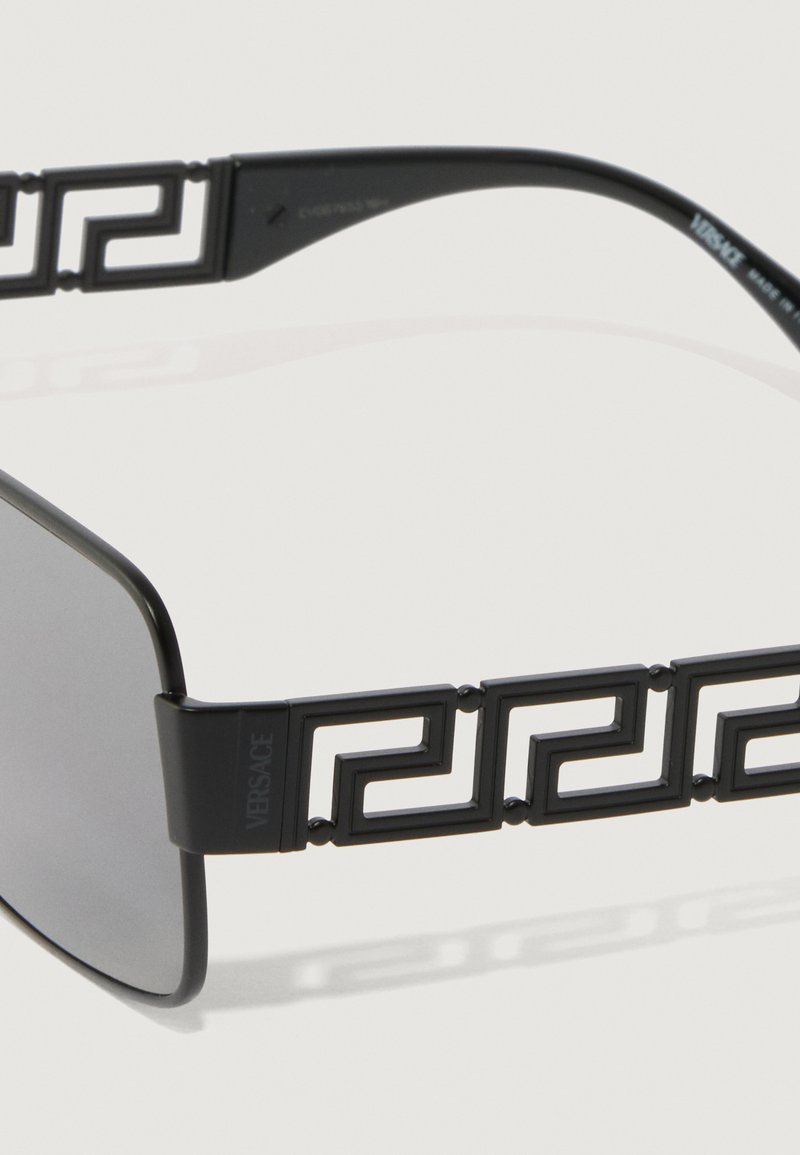 Svarta solglasögon med rektangulär form, med ett geometriskt mönster på glasögonens tempel. Linserna är mörkgrå, och ramen verkar vara av plast.