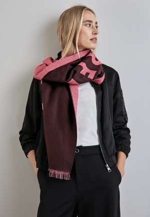 Sciarpa bordeaux e rosa con motivo a quadri e bordi sfrangiati, indossata sopra un giubbotto nero, caratterizzata da una texture morbida e un drappeggio a strati.