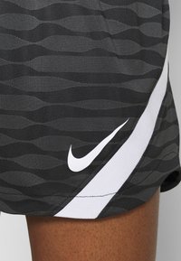 Svarta och grå sportshorts med ett vågmönster, med en vit Nike-logotyp på nedre sidan och en kontrasterande vit accentlinje.