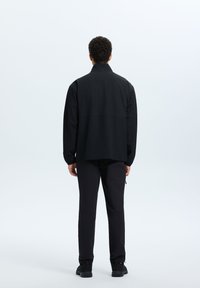 Black lightweight jacket with a stand-up collar, relaxed fit, and long sleeves, paired with matching black trousers and dark footwear.