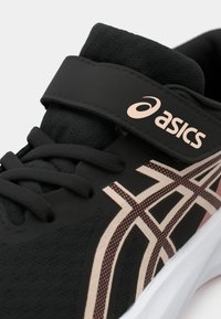 Μαύρο αθλητικό παπούτσι με υφή στην επάνω πλευρά, διαθέτοντας φαρδύ ιμάντα με βέλκρο, κορδόνια και λευκή σόλα. Διακοσμήσεις σε ροζ και μπεζ γραφικό μοτίβο.