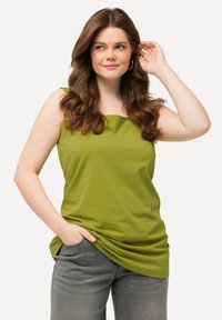 Top senza maniche verde realizzato in tessuto morbido, caratterizzato da una vestibilità rilassata con dettagli drappeggiati sul colletto, abbinato a jeans grigi.