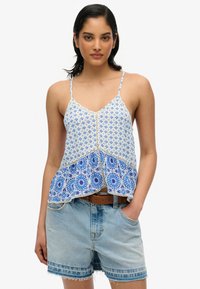 Top sin mangas de color azul con un estampado, que presenta un intrincado bordado floral en el dobladillo, combinado con pantalones cortos de mezclilla claros.