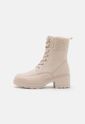 Beige leather ankle boots with a textured fur cuff, lace-up front, and chunky block heel for stability. Notable stitching detail on the toe.