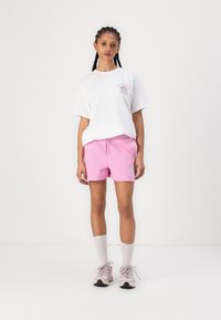 Camiseta de algodón blanca con estampado gráfico, combinada con pantalones cortos de algodón rosa. Los accesorios incluyen calcetas blancas hasta la rodilla y zapatillas rosa claro.