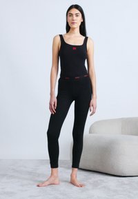 Body noir ajusté avec bretelles réglables, présentant un logo rouge au centre ; assorti à des leggings noirs avec une ceinture rouge.