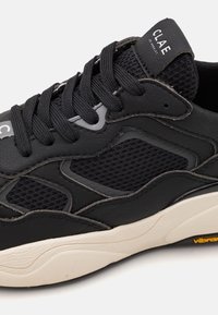 Black sneaker with a mesh and leather upper, featuring a textured sole and contrasting white midsole. CLAE logo on the tongue.