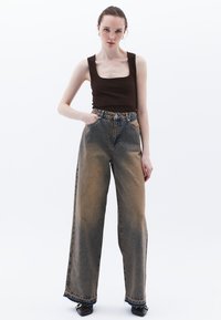 Jeans a gamba larga, blu scoloriti, con vita alta, dotati di chiusura a bottone, tasche e orli sfrangiati. Abbinati a un top senza maniche marrone.
