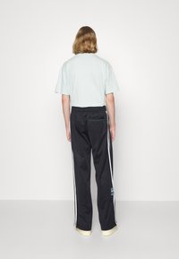 Ljusblå kortärmad t-shirt i kombination med svarta byxor med vita sidstriper, elastisk midja och en bakficka med en teal-accent.