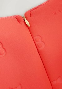 Koralo zip-up drabužis su tekstūruota apdaila. Savybė - auksinė užtrauktuko stūmoklis ir įspaudžiami užrašai ant audinio. Detali apžvalga prie kaklo.