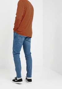 Långärmad orange och svart randig skjorta i kombination med blå jeans och svarta sneakers, med en avslappnad passform och mjuk textur.