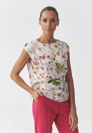 Floral-patterned blouse in light pink fabric, featuring short sleeves and a rounded neckline, paired with vibrant pink trousers.