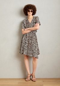 Robe imprimée léopard avec des manches courtes, un décolleté en V et une taille froncée. Portée avec des sandales à talons beiges sur un sol en bois clair.