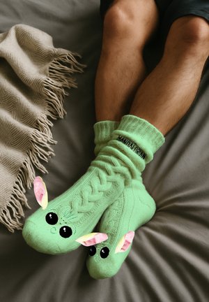 Green knitted socks with a cable pattern, featuring cartoon character face designs, including large eyes and ear accents.