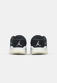 Baskets en daim noir avec semelles en caoutchouc blanches, arborant un logo signature sur le talon et une texture lisse sur toute la tige.