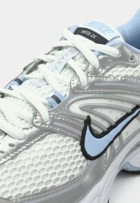 Jasnoszare sneakersy z siateczkową górą, czarnymi i niebieskimi akcentami, białymi sznurówkami, wyściełanym kołnierzem oraz wzorzystymi detalami po bokach.