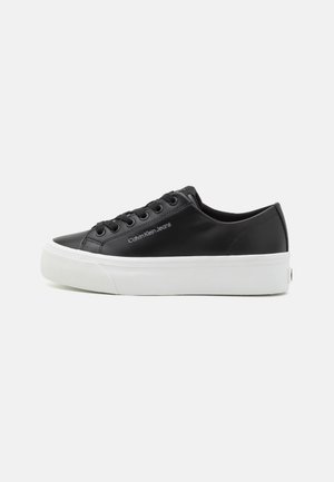 Baskets en cuir noir basses avec semelle épaisse en caoutchouc blanc, lacets à l'avant et logo "Calvin Klein Jeans" sur le côté.