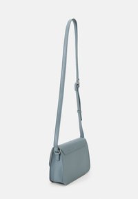 Piccola borsa a tracolla blu chiaro con lunga tracolla regolabile e chiusura a pattina su uno sfondo bianco.