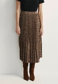 Brązowa plisowana spódnica midi w czarne kropki, z wysokim stanem i miękką teksturą materiału. Zestawiona z brązowymi zamszowymi botkami do kolan.