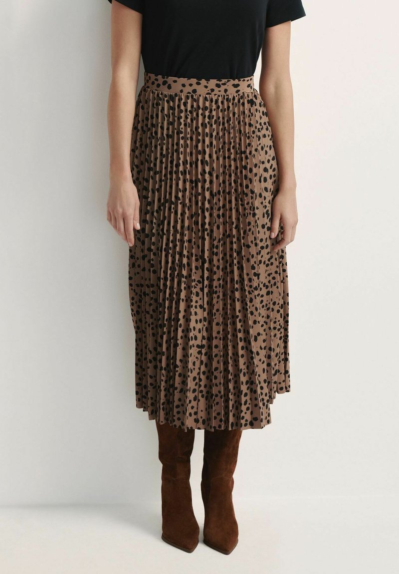 Brązowa plisowana spódnica midi w czarne kropki, z wysokim stanem i miękką teksturą materiału. Zestawiona z brązowymi zamszowymi botkami do kolan.