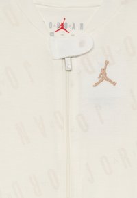 Cream zip-up bodysuit featuring embossed "JORDAN" text, subtle texture, and a tan embroidered Jumpman logo on the front.