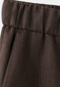 Ceinture élastique sur tissu texturé marron foncé, montrant des coutures froncées et des détails de couture.