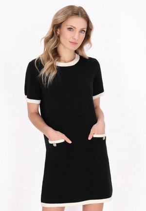 Abito corto nero a maniche corte con bordi bianchi, dotato di due tasche frontali con dettagli a bottoni. Texture lavorata a maglia, vestibilità comoda, lunghezza al ginocchio.