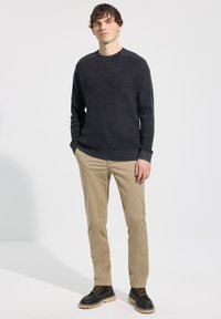 Pull gris foncé à côtes, pantalon beige et bottes noires. Le pull présente un col rond, un tissu texturé, et le pantalon est ajusté.