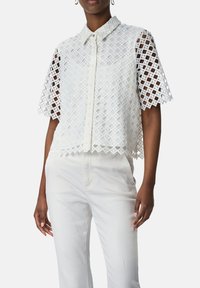 Witte blouse met korte mouwen en een roostervormig ontwerp, knoopsluiting en ronde kraag, gecombineerd met witte broek.