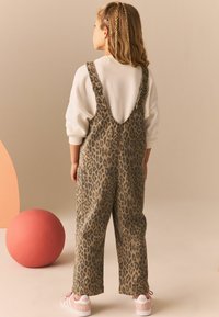 Pantalones de tirantes de estampado de leopardo con tirantes ajustables, material de mezcla de algodón, corte holgado, combinados con zapatillas rosa claro sobre un fondo neutro.