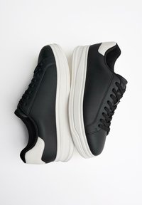 Schwarze Ledersneaker mit schwarzen Schnürsenkeln, weißer Gummisohle und kontrastierenden weißen Akzenten an der Ferse; glatte Oberfläche mit subtilen Nähdetails.