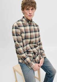 Beige geruite blouse met donkerrode en marineblauwe accenten, met een knoopsluiting kraag en lange mouwen, gecombineerd met lichtblauwe jeans.