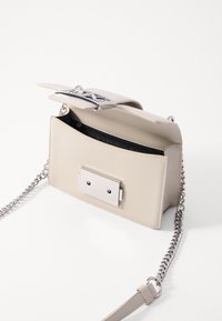 Beige läderhandväska med ett silverfärgat metallspänne, en kedjeslunga, en strukturerad yta och ett innerfack. Kompakt rektangulär form.