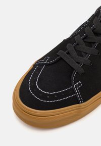 Baskets en suède noir avec coutures blanches, lacets noirs et semelle en caoutchouc texturé couleur gomme. Vue rapprochée mettant en évidence les détails de conception de la tige.