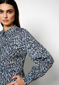 Langärmliges Hemd in einem blauen und cremefarbenen abstrakten Muster, mit einem Kragen und Knopfdetails, aus einem leichten, strukturierten Stoff gefertigt.