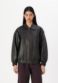 Black leather jacket with a wide collar, zip fastening, and elasticated cuffs; features vertical stitching details and a loose fit.