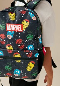 Marvel-inspirerad ryggsäck med svart tyg och färgglada superhjälteansikten, inklusive Spider-Man, Iron Man och Hulk. Röd logotypdetalj.