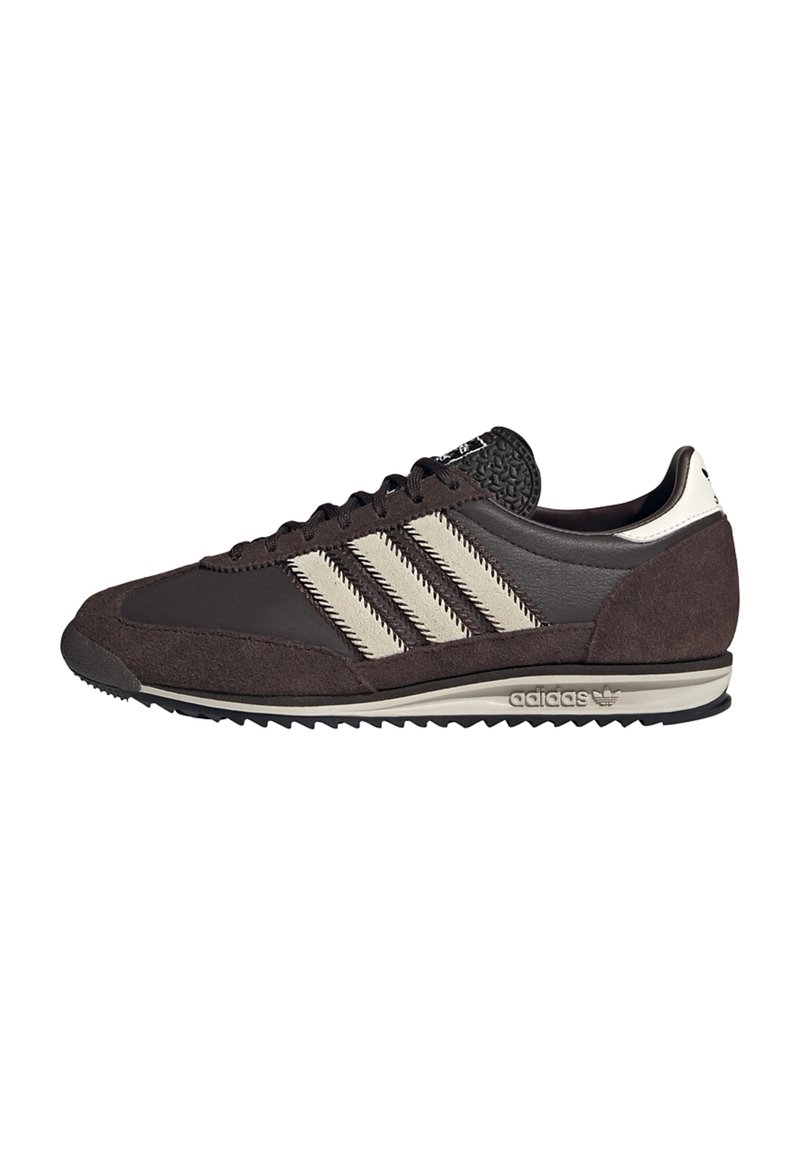 Niske tamno smeđe Adidas tenisice s svijetlosmešastim prugama, izrađene od antilopa i kože, s teksturiranim jezikom i nazubljenim uzorkom na potplatu.