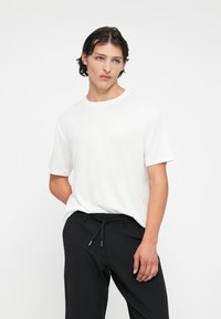 Tricou alb din bumbac, cu mâneci scurte și guler rotund, asortat cu pantaloni negri, cu talie elastică și șnur.