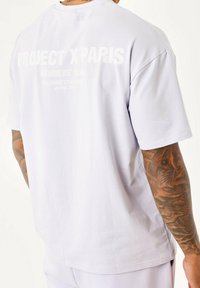 Camiseta de manga corta morada clara con gráfico en la parte trasera que dice "PROJECT X PARIS" y "DISEÑANDO STREETWEAR desde 2015". Material de algodón.