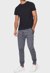 Schwarzes Rundhals-T-Shirt, kombiniert mit grauen Jogginghosen mit Kniefalten und elastischen Bündchen, ergänzt durch weiße Turnschuhe.